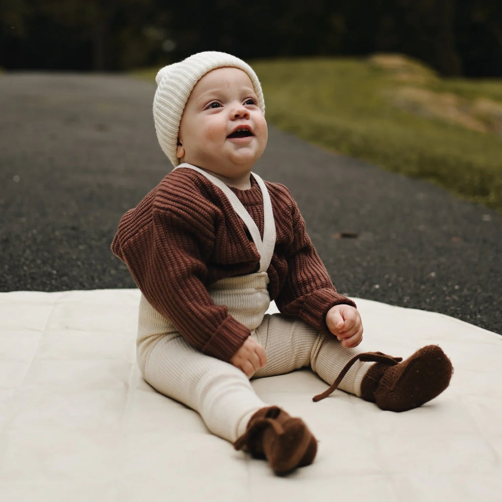 Un petit bébé dans un parc qui porte un pull en tricot couleur cacao