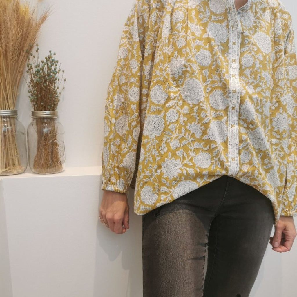 Une élégante blouse Bonheur du jour Paris "Oriana" de couleur jaune absynthe, portée par une femme . La blouse, d'une forme fluide et aérienne, est fabriquée en mousseline de coton et possède des manches courtes bouffantes et un col montant. 
