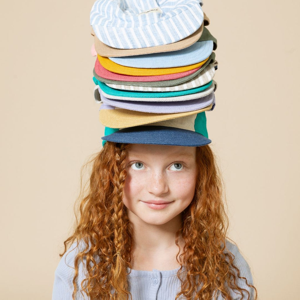 Une petite fille rousse d'environ 8 ans portant en équilibre les casquettes en lin de la marque Caribou